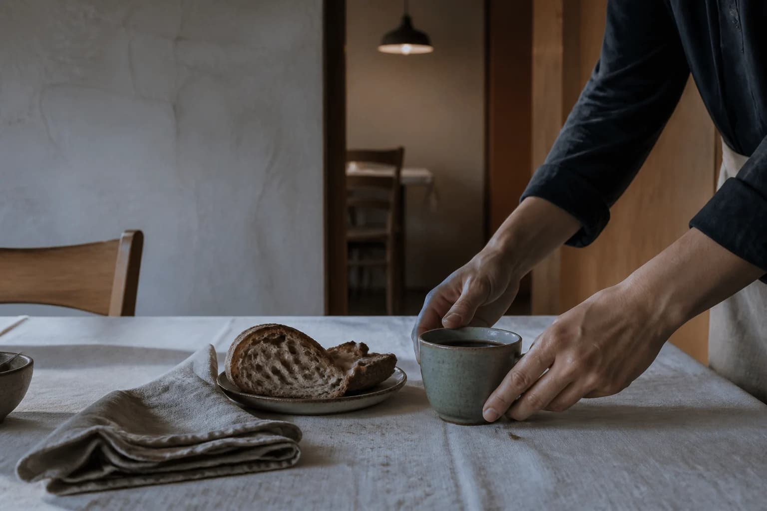 Una persona sirve café y pan sobre una mesa de lino.