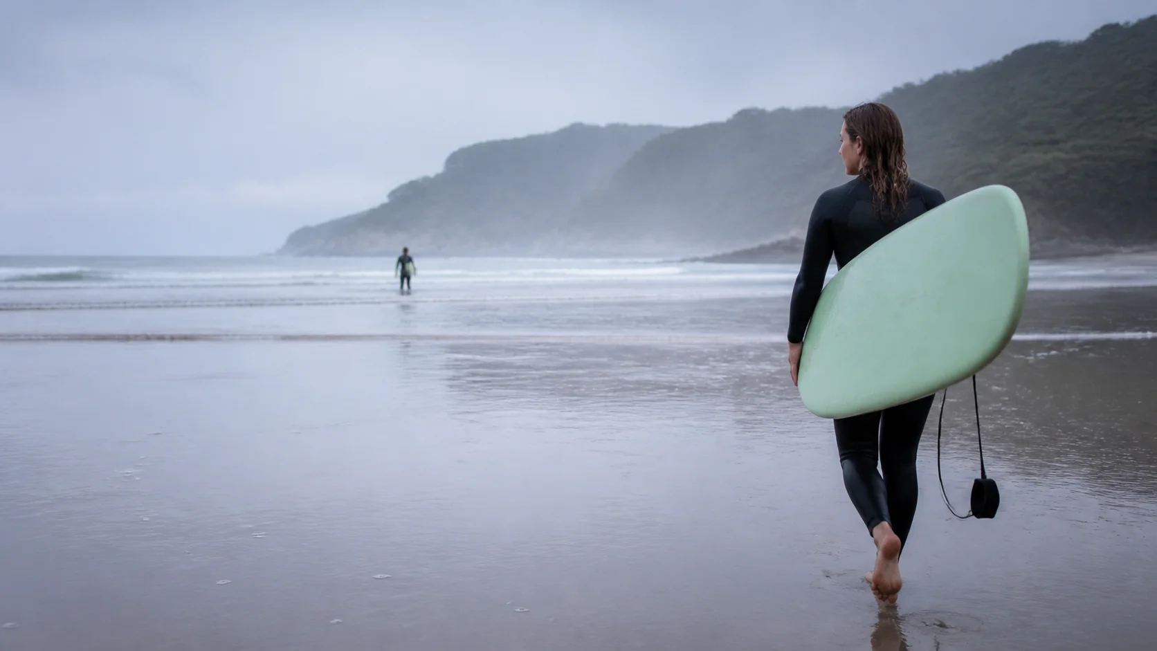 Una mujer camina hacia el agua con una tabla de surf.